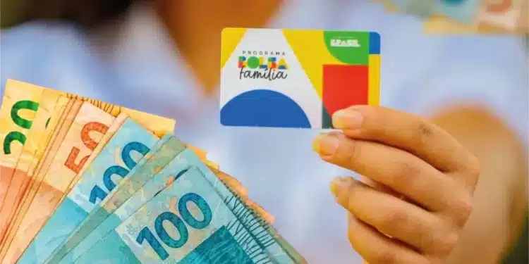 Pessoa segura cartão do Bolsa Família ao lado de cédulas de dinheiro, em referência a novo auxílio aprovado para beneficiários do programa.