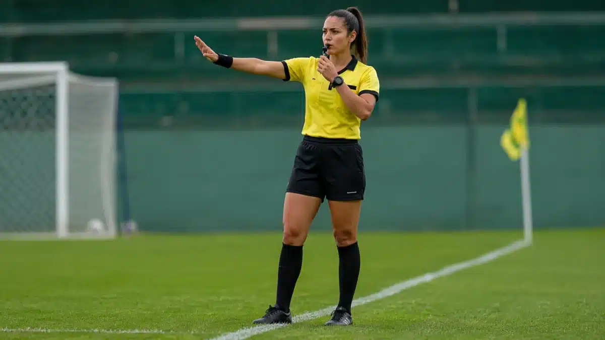 Origem do termo árbitro Árbitra em campo sinalizando durante partida esportiva, representando a origem da palavra “árbitro”.