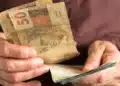 Pessoa segura cédulas de real, representando o pagamento do BPC previsto para agosto de 2026.