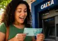 Mulher confere uma nota de R$ 100 após sacar dinheiro em caixa eletrônico, representando o pagamento do 3º lote da restituição do Imposto de Renda.