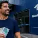 Homem segura cédulas de real em frente a uma unidade da Receita Federal, representando o pagamento de R$ 500 milhões a contribuintes.