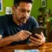 Homem utilizando celular para realizar pagamento digital enquanto cédula de dinheiro aparece desfocada em mesa, representando a pensão alimentícia via Pix.