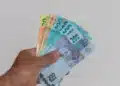 Mulher segurando dinheiro em espécie, com foco em cédulas de real, representando o pagamento de R$ 2.486.