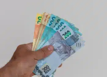 Mulher segurando dinheiro em espécie, com foco em cédulas de real, representando o pagamento de R$ 2.486.
