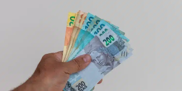 Mulher segurando dinheiro em espécie, com foco em cédulas de real, representando o pagamento de R$ 2.486.