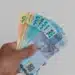 Mulher segurando dinheiro em espécie, com foco em cédulas de real, representando o pagamento de R$ 2.486.