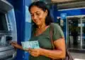 Mulher retirando o pagamento de benefício do INSS em caixa eletrônico de uma agência bancária, representando os depósitos referentes a julho.