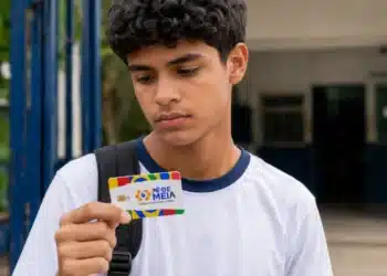 Estudante observa o cartão do Pé-de-Meia em frente à escola, representando a suspensão dos pagamentos em julho.