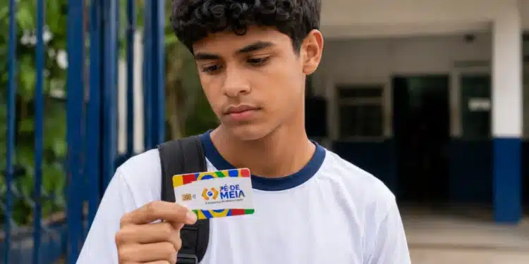 Estudante observa o cartão do Pé-de-Meia em frente à escola, representando a suspensão dos pagamentos em julho.