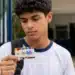 Estudante observa o cartão do Pé-de-Meia em frente à escola, representando a suspensão dos pagamentos em julho.