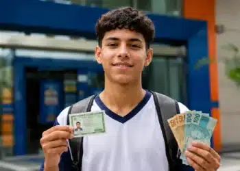 Estudante segura documento e notas de real, representando o pagamento das parcelas do Pé-de-Meia em agosto de 2026.