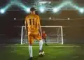 Jogador se prepara para cobrar pênalti diante do goleiro em estádio de futebol iluminado.