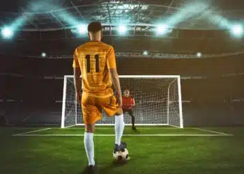 Jogador se prepara para cobrar pênalti diante do goleiro em estádio de futebol iluminado.