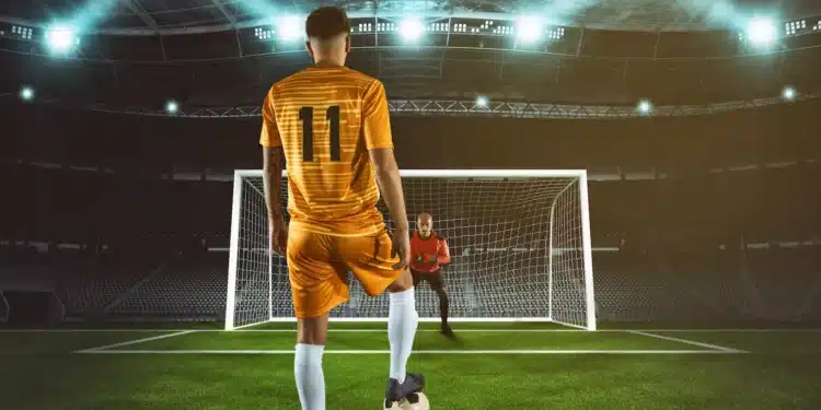 Jogador se prepara para cobrar pênalti diante do goleiro em estádio de futebol iluminado.