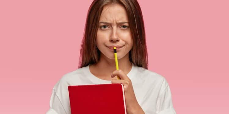 Imagem ilustrativa de jovem segurando um caderno vermelho e um lápis junto ao rosto, com expressão de desconfiança, em referência à dúvida sobre o plural de irmão