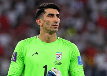 Goleiro iraniano com uniforme verde, luvas e expressão séria durante partida mundial.