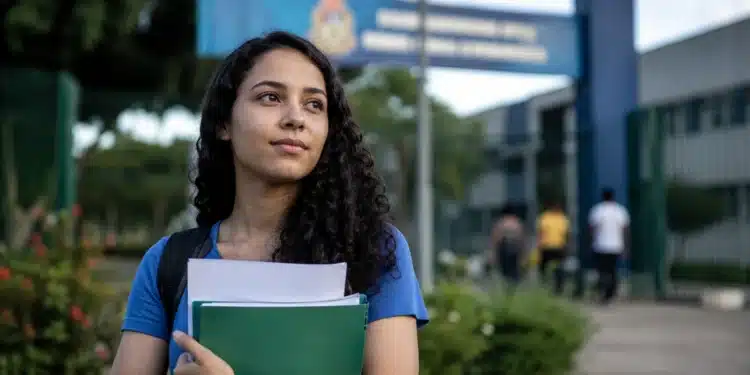 Jovem universitária segura documentos diante de uma instituição de ensino, representando a prorrogação das inscrições do Fies 2026.2.
