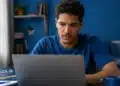 Jovem estudando pelo computador ao lado de um livro do Encceja, representando a dúvida sobre fazer a prova pela internet em 2026.