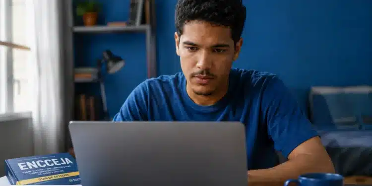 Jovem estudando pelo computador ao lado de um livro do Encceja, representando a dúvida sobre fazer a prova pela internet em 2026.