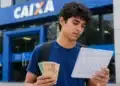 Estudante consulta o calendário do próximo pagamento do Pé-de-Meia 2026 em frente a uma agência da Caixa, representando a nova liberação do benefício.