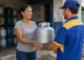 Mulher recebe um botijão de gás de um entregador em uma revenda, em referência à recarga do Gás do Povo de julho.