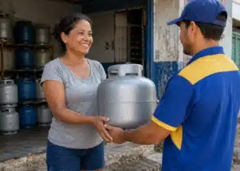Mulher recebe um botijão de gás de um entregador em uma revenda, em referência à recarga do Gás do Povo de julho.
