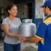 Mulher recebe um botijão de gás de um entregador em uma revenda, em referência à recarga do Gás do Povo de julho.