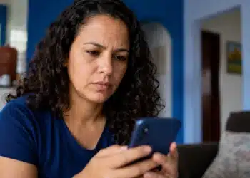 Mulher mexendo no celular, representando a tentativa de recuperar o acesso ao Facebook sem lembrar o e-mail e a senha.