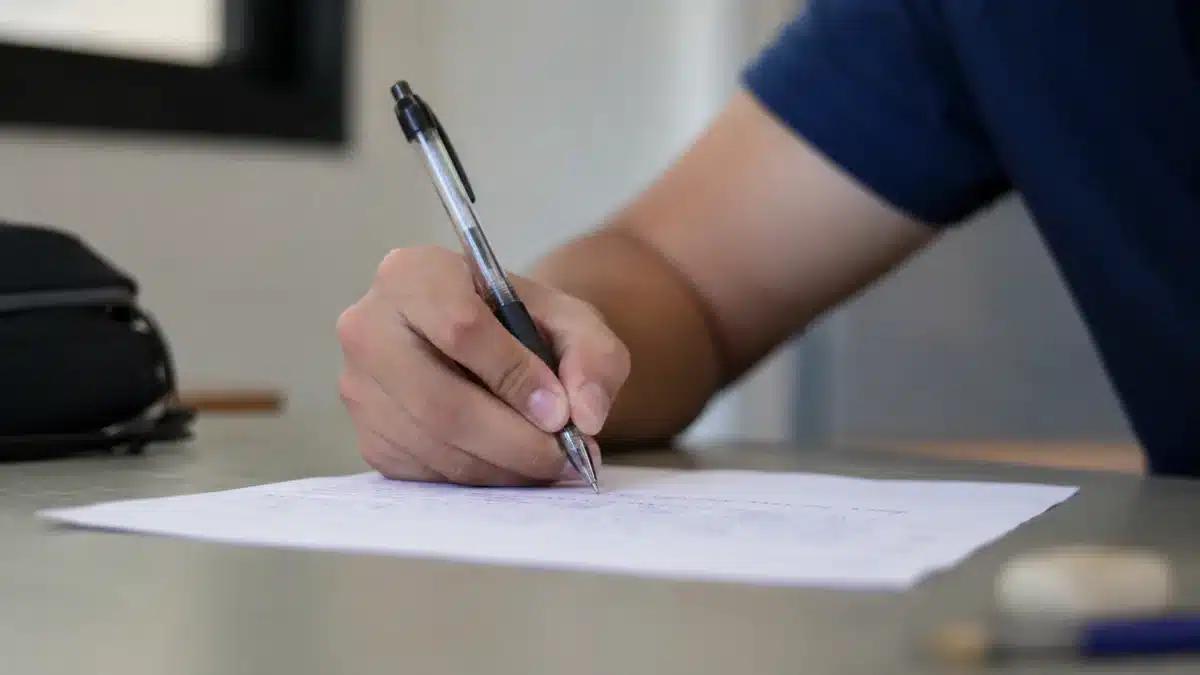 Mão de candidato escrevendo uma redação, representando o texto produzido na prova do concurso de Escriturário do Banco do Brasil.