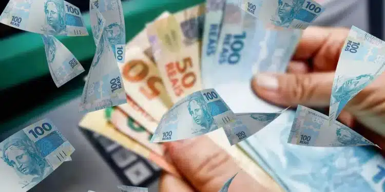 Cédulas de reais em mãos sobre imagem de dinheiro, representando a restituição do Imposto de Renda 2026, que libera lote regular e especial.