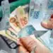 Cédulas de reais em mãos sobre imagem de dinheiro, representando a restituição do Imposto de Renda 2026, que libera lote regular e especial.