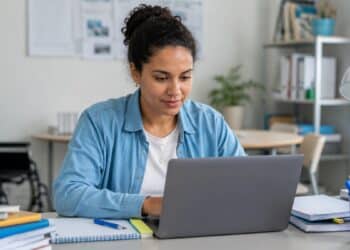 Participante consulta o notebook em mesa de estudos, com cadeira de rodas ao fundo, cena da consulta ao resultado dos recursos de atendimento especializado da PND 2026 pelo Sistema PND
