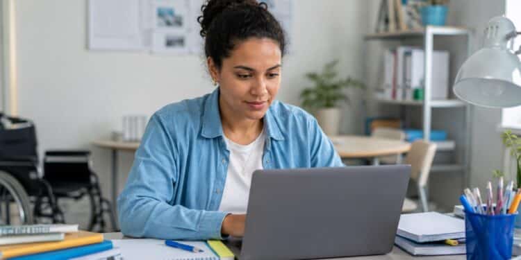 Participante consulta o notebook em mesa de estudos, com cadeira de rodas ao fundo, cena da consulta ao resultado dos recursos de atendimento especializado da PND 2026 pelo Sistema PND