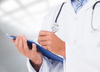 Mãos de médico preenchendo prancheta, representando os próximos passos do Revalida 2026/2