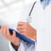 Mãos de médico preenchendo prancheta, representando os próximos passos do Revalida 2026/2