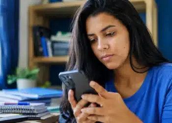 Jovem universitária consulta o celular em casa, representando a espera pelo resultado dos pré-selecionados do Fies 2026.2.