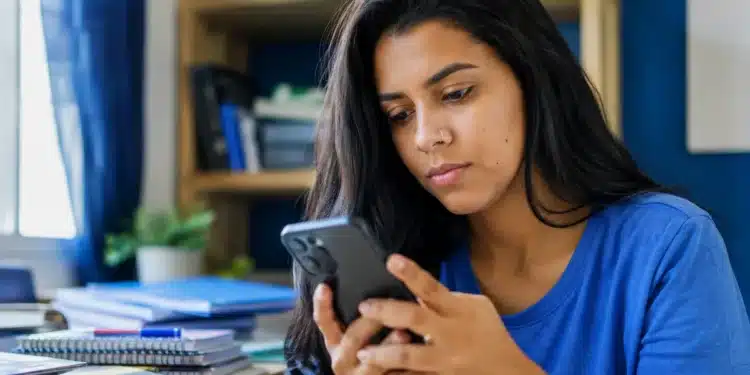 Jovem universitária consulta o celular em casa, representando a espera pelo resultado dos pré-selecionados do Fies 2026.2.