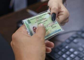 Pessoa segurando uma carteira de identidade no modelo antigo diante do rosto
