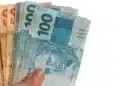 Mãos segurando cédulas de real brasileiro, ilustrando a liberação para solicitação do Saque Calamidade do FGTS em 2026.