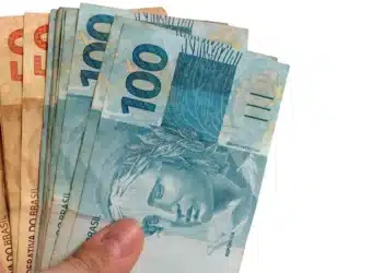 Mãos segurando cédulas de real brasileiro, ilustrando a liberação para solicitação do Saque Calamidade do FGTS em 2026.