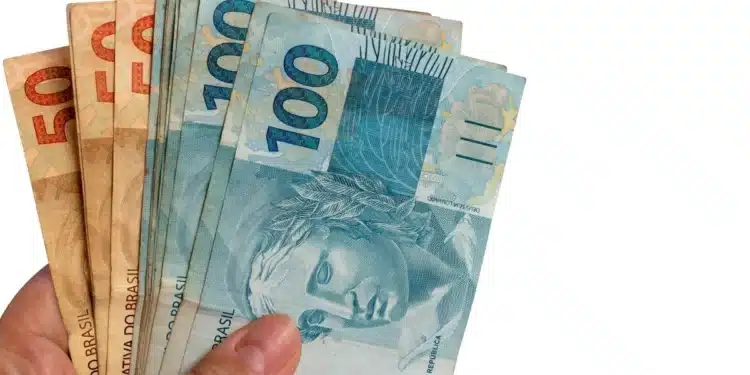 Mãos segurando cédulas de real brasileiro, ilustrando a liberação para solicitação do Saque Calamidade do FGTS em 2026.