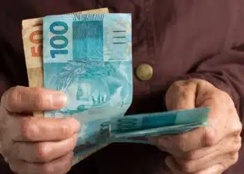 Pessoa segurando cédulas de real, representando a solicitação de até R$ 6.220 do FGTS, disponível a partir de 29 de julho de 2026.