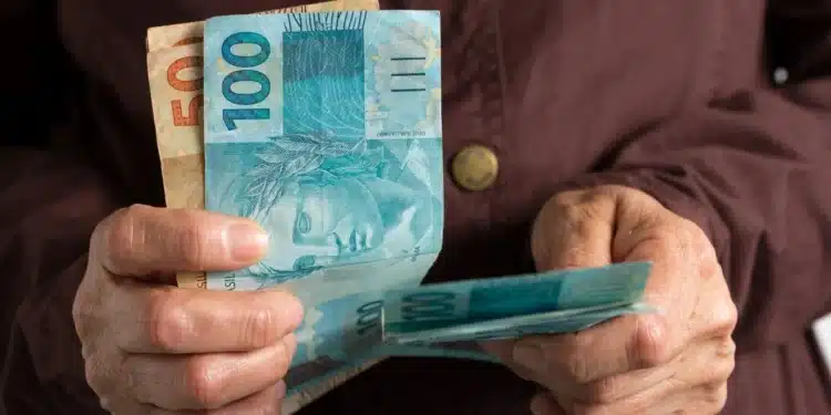 Pessoa segurando cédulas de real, representando a solicitação de até R$ 6.220 do FGTS, disponível a partir de 29 de julho de 2026.