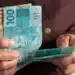 Pessoa segurando cédulas de real, representando a solicitação de até R$ 6.220 do FGTS, disponível a partir de 29 de julho de 2026.