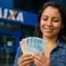 Mulher conta cédulas em frente a uma agência da Caixa, representando a liberação de mais de R$ 6 mil por meio do saque do FGTS.