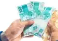 Notas de real em mãos simbolizando o saque de R$ 6,2 mil do FGTS liberado pela Caixa para moradores de 18 cidades.