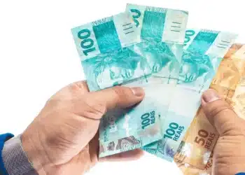 Notas de real em mãos simbolizando o saque de R$ 6,2 mil do FGTS liberado pela Caixa para moradores de 18 cidades.