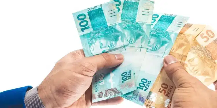 Notas de real em mãos simbolizando o saque de R$ 6,2 mil do FGTS liberado pela Caixa para moradores de 18 cidades.