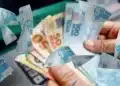 Mãos segurando notas de real para representar o saque de R$ 6.220 do FGTS, liberado para moradores de seis estados.