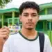 Jovem estudante brasileiro segurando o cartão do programa Pé-de-Meia em frente a uma escola pública.
